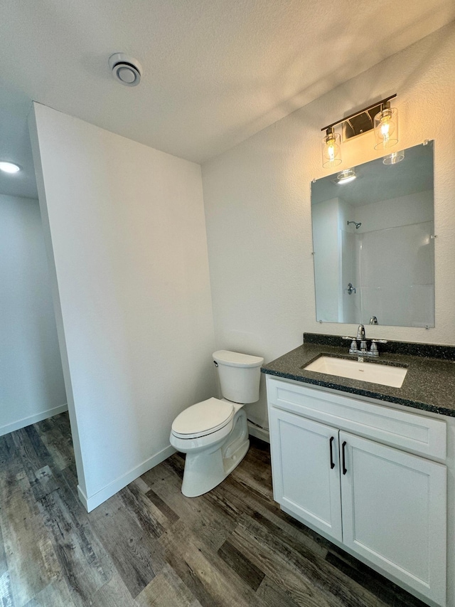 bathroom with a textured ceiling, wood-type flooring, vanity, toilet, and walk in shower