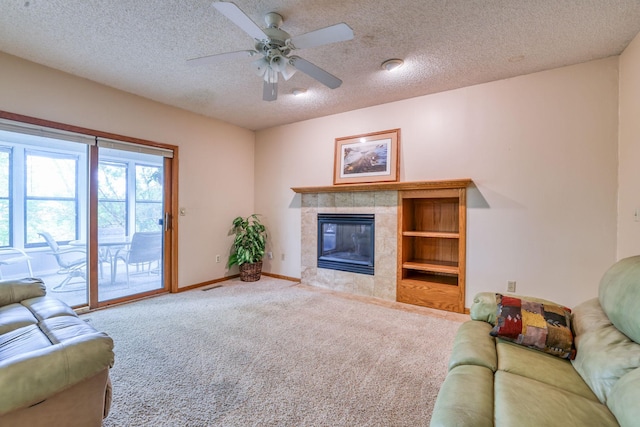 living room featuring a tiled fireplace, ceiling fan, a textured ceiling, and carpet