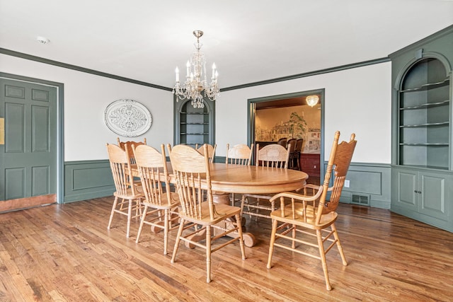 dining area featuring a notable chandelier, built in features, a decorative wall, crown molding, and light wood-type flooring