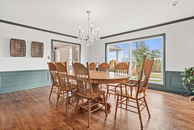 dining room with a wealth of natural light, an inviting chandelier, crown molding, and a wainscoted wall