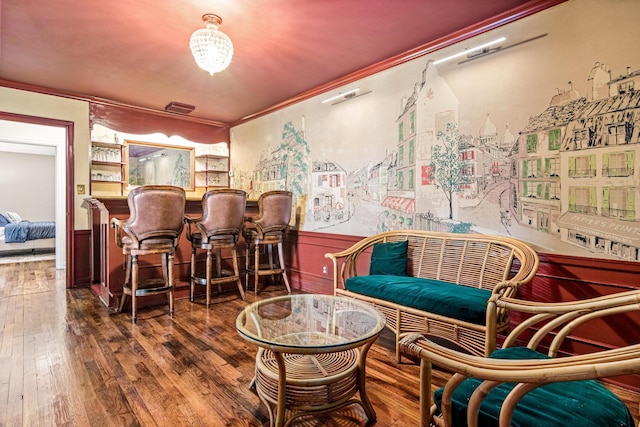 living area featuring a wainscoted wall, crown molding, a bar, and hardwood / wood-style floors