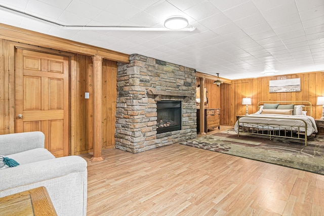 bedroom with wooden walls, a stone fireplace, and wood finished floors