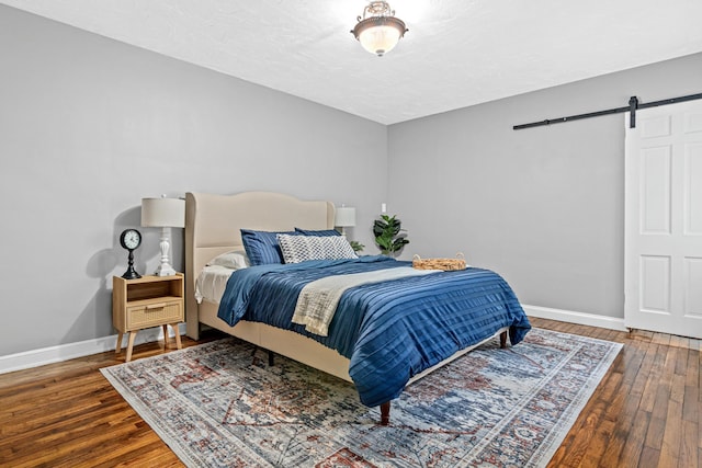bedroom with baseboards, a barn door, and hardwood / wood-style flooring