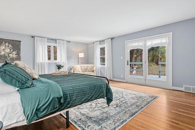 bedroom with multiple windows, visible vents, wood finished floors, and access to exterior