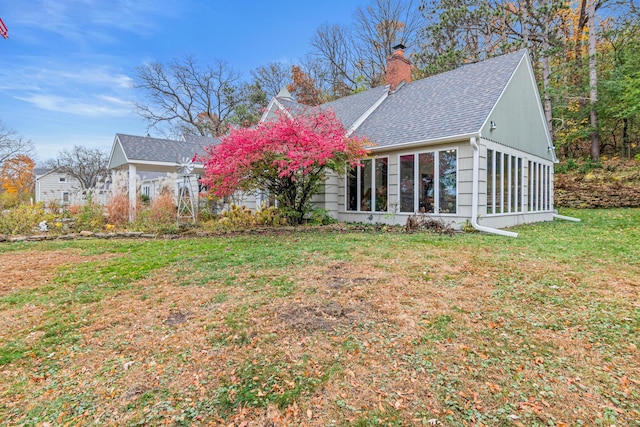 back of property with a sunroom, a yard, roof with shingles, and a chimney