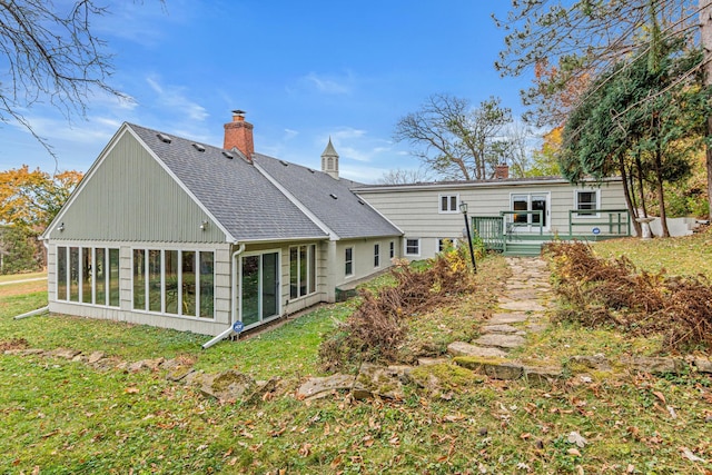 back of property with roof with shingles, a wooden deck, a chimney, a lawn, and a sunroom