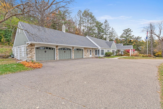 ranch-style house featuring roof with shingles, an attached garage, stone siding, driveway, and a chimney