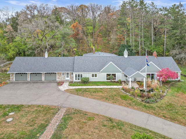 view of front of house featuring roof with shingles, driveway, a garage, a front lawn, and a chimney