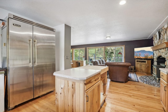 kitchen featuring light wood-type flooring, stainless steel built in refrigerator, a textured ceiling, light brown cabinets, and a kitchen island