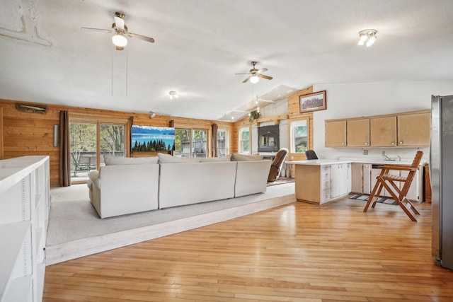 unfurnished living room with light wood-type flooring, vaulted ceiling, ceiling fan, and wood walls