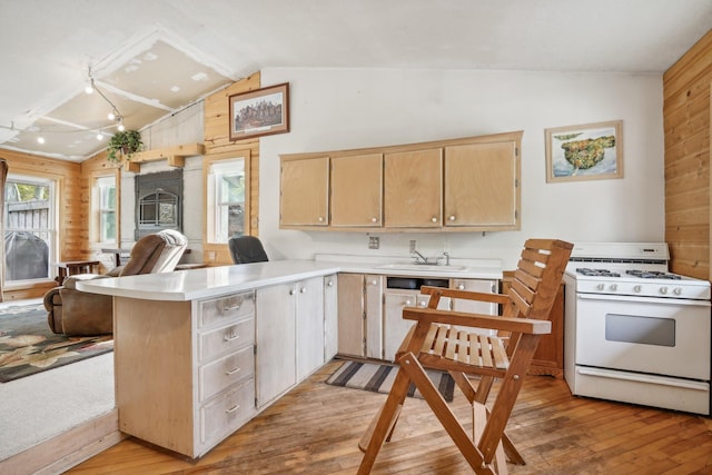 kitchen with white gas stove, light brown cabinets, light wood-type flooring, and wooden walls