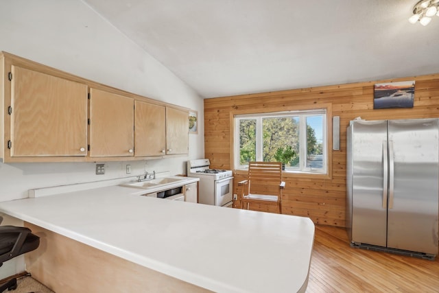 kitchen featuring stainless steel refrigerator, white gas range, kitchen peninsula, light hardwood / wood-style floors, and wooden walls