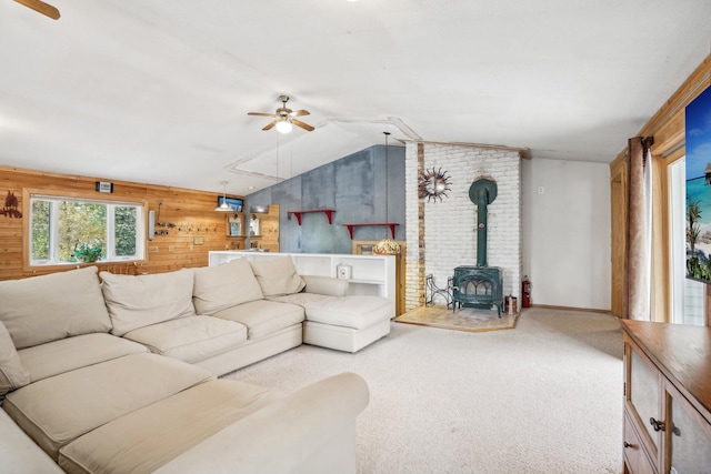 living room with wood walls, a wood stove, lofted ceiling, ceiling fan, and light colored carpet