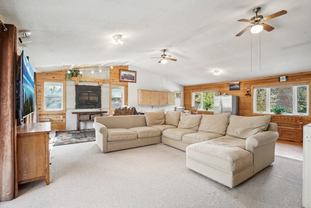 carpeted living room featuring vaulted ceiling, ceiling fan, and wood walls