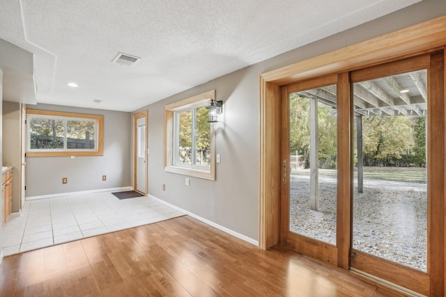 doorway to outside with a wealth of natural light, a textured ceiling, and light wood-type flooring