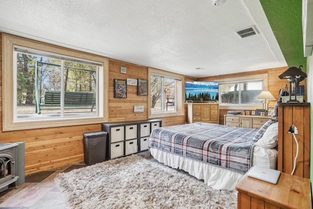 bedroom with multiple windows, a textured ceiling, and a wood stove