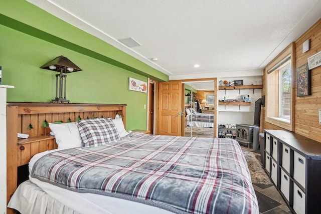 bedroom featuring wood walls, a wood stove, and a textured ceiling