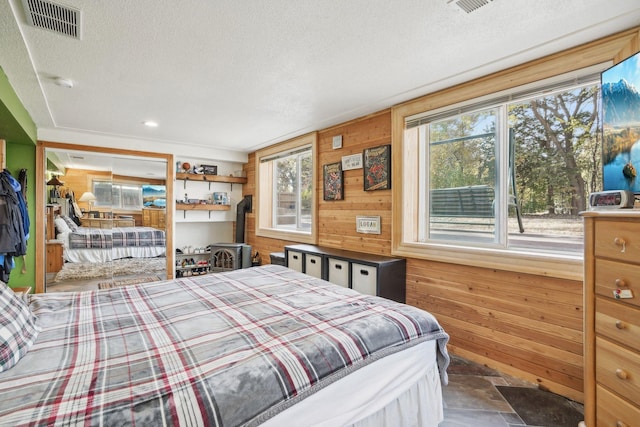 bedroom with a textured ceiling, a wood stove, and wood walls