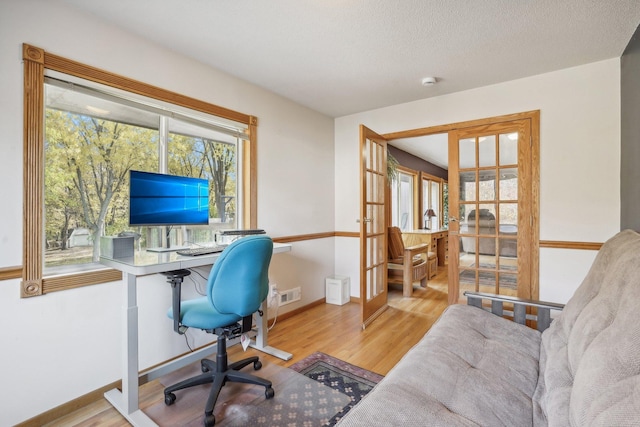 office with french doors, light wood-type flooring, and a textured ceiling