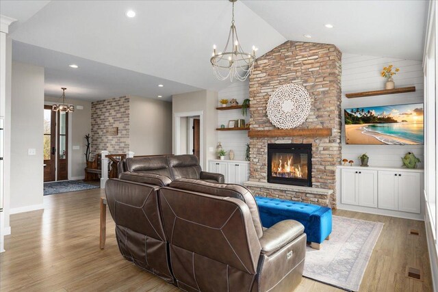 living room with lofted ceiling, a chandelier, a fireplace, light hardwood / wood-style floors, and wooden walls