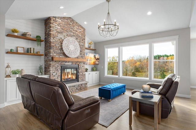 living room featuring wood walls, a large fireplace, lofted ceiling, a notable chandelier, and light hardwood / wood-style flooring