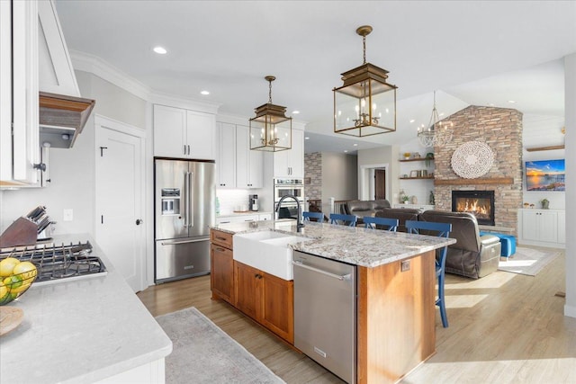 kitchen featuring a kitchen island with sink, stainless steel appliances, light stone countertops, white cabinets, and a fireplace