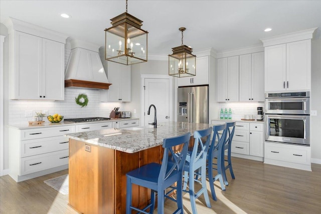 kitchen featuring appliances with stainless steel finishes, light hardwood / wood-style flooring, a center island with sink, and premium range hood