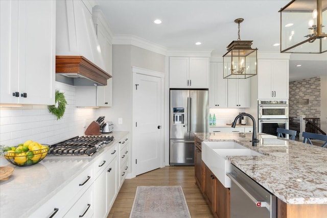 kitchen with white cabinets, a center island with sink, custom range hood, pendant lighting, and stainless steel appliances