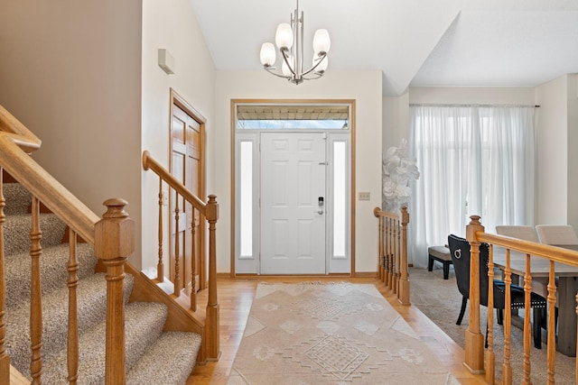 foyer featuring baseboards, light wood-style flooring, a chandelier, and stairway