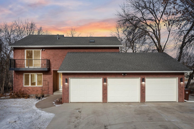 view of front of home featuring brick siding, a balcony, driveway, and a shingled roof