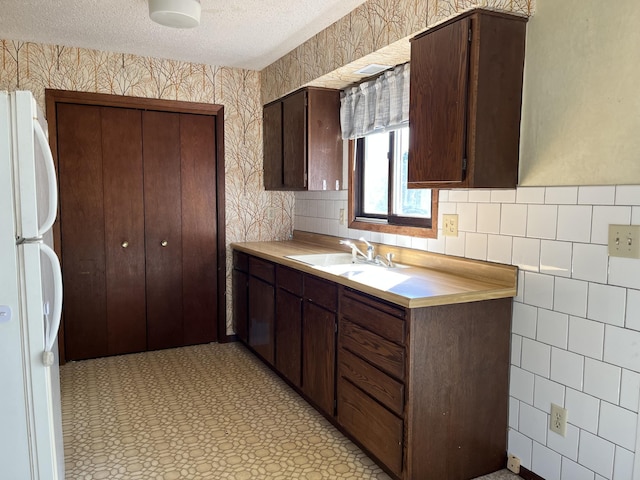 kitchen with dark brown cabinetry, sink, white fridge, and a textured ceiling