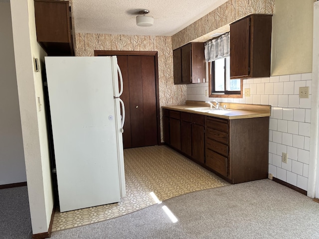 kitchen with sink, a textured ceiling, dark brown cabinetry, white fridge, and light colored carpet