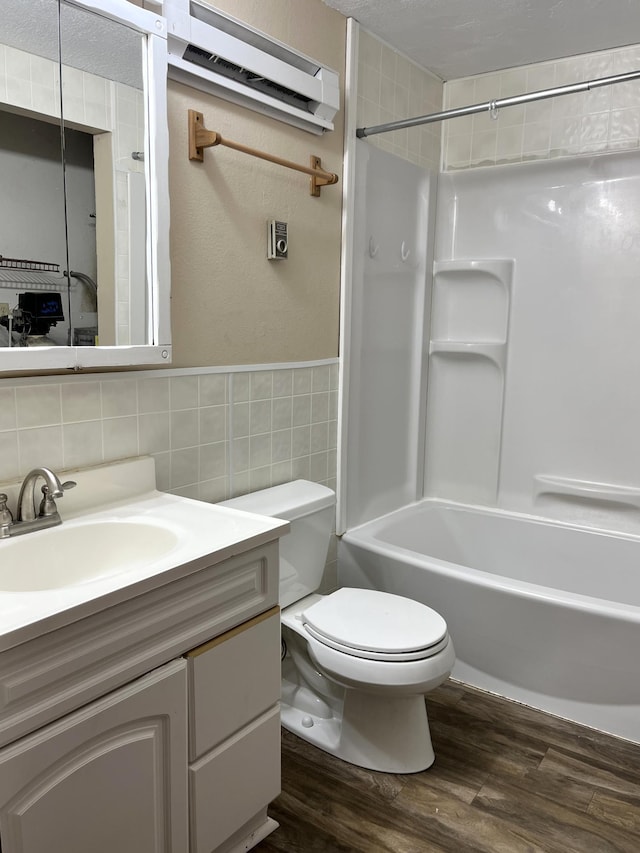 full bathroom with hardwood / wood-style flooring, toilet, shower / bathtub combination, vanity, and tile walls