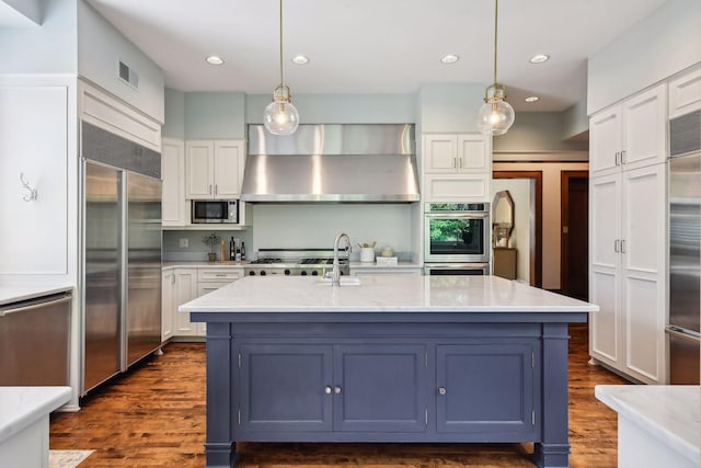 kitchen featuring exhaust hood, built in appliances, pendant lighting, and white cabinetry