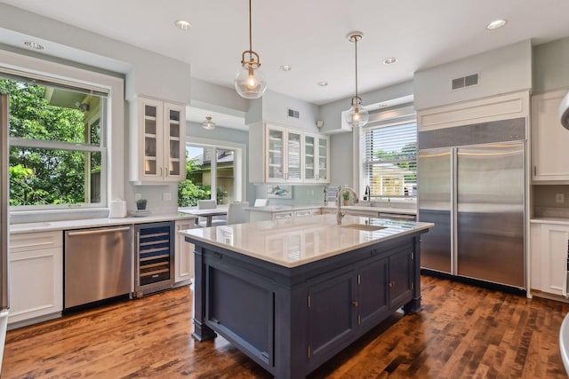 kitchen featuring white cabinets, stainless steel appliances, beverage cooler, and a wealth of natural light