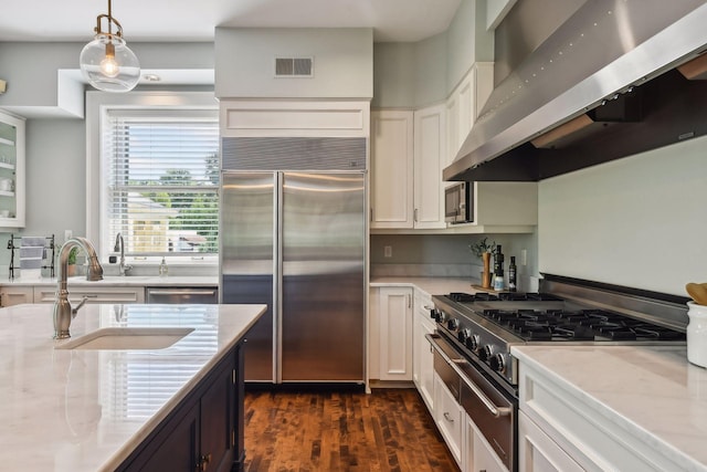 kitchen featuring wall chimney range hood, high quality appliances, dark wood-type flooring, pendant lighting, and white cabinetry