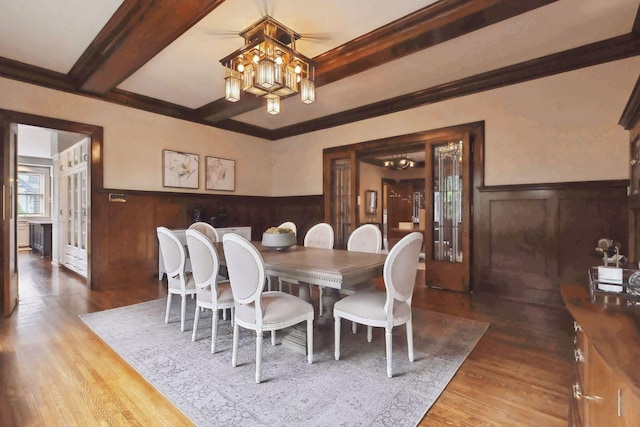 dining room with a notable chandelier, hardwood / wood-style flooring, ornamental molding, and beam ceiling