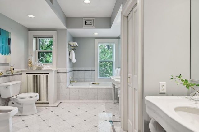 bathroom featuring a wealth of natural light, toilet, a relaxing tiled tub, and radiator heating unit