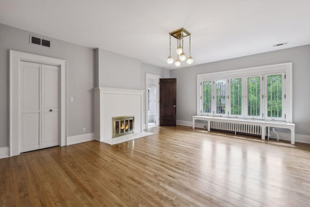 unfurnished living room with a chandelier, light hardwood / wood-style flooring, and radiator