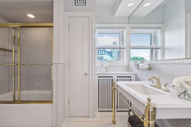 bathroom featuring tile patterned floors, sink, bath / shower combo with glass door, tile walls, and radiator heating unit