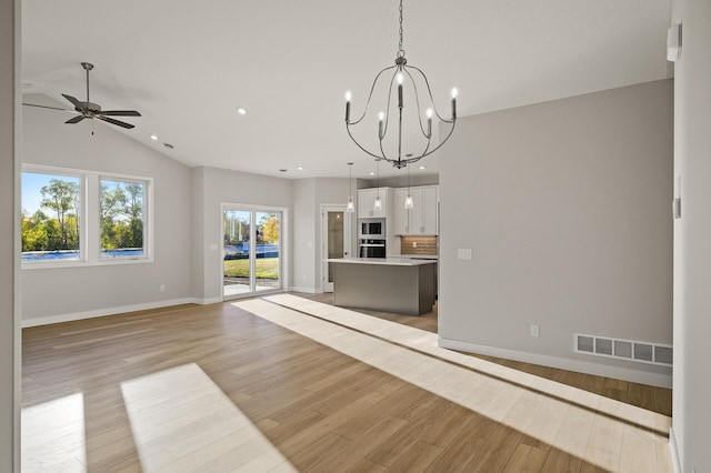 unfurnished living room with lofted ceiling, ceiling fan with notable chandelier, and light wood-type flooring