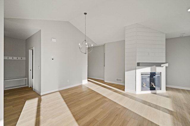 unfurnished living room with lofted ceiling, hardwood / wood-style floors, a notable chandelier, and a large fireplace