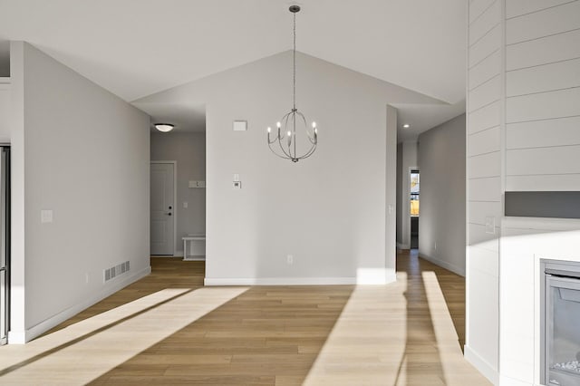 unfurnished dining area with an inviting chandelier, lofted ceiling, a fireplace, and light wood-type flooring