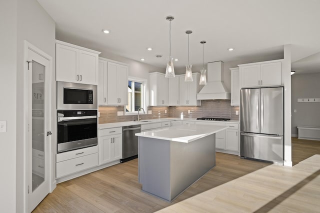 kitchen with appliances with stainless steel finishes, a kitchen island, white cabinetry, pendant lighting, and custom exhaust hood