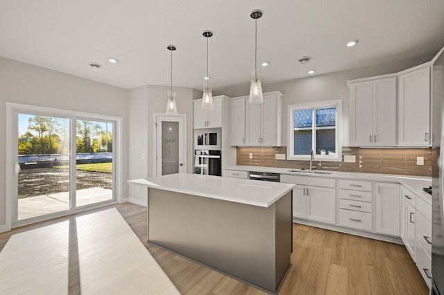 kitchen with appliances with stainless steel finishes, sink, a kitchen island, backsplash, and white cabinetry