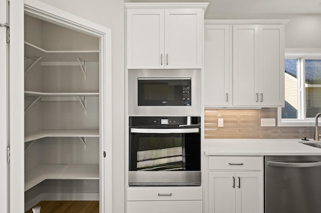 kitchen featuring stainless steel dishwasher, sink, decorative backsplash, and white cabinetry