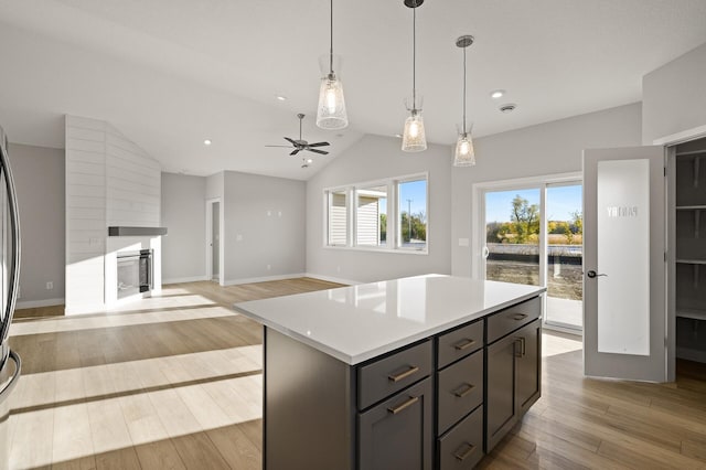 kitchen featuring lofted ceiling, hanging light fixtures, ceiling fan, a kitchen island, and light hardwood / wood-style floors