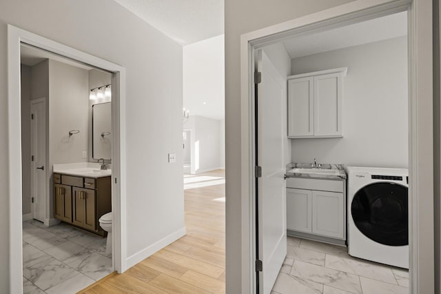 clothes washing area with cabinets, light hardwood / wood-style flooring, washer / clothes dryer, and sink