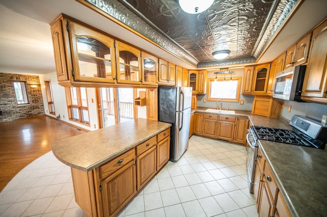 kitchen with brick wall, stainless steel appliances, a raised ceiling, sink, and light hardwood / wood-style flooring