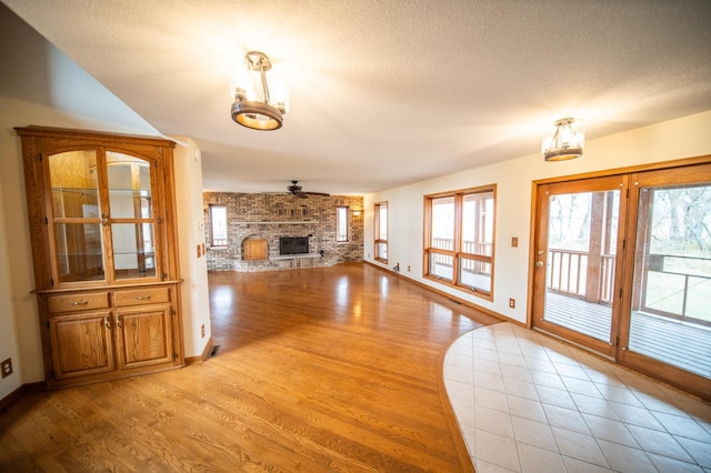 unfurnished living room featuring ceiling fan, a fireplace, a textured ceiling, and light wood-type flooring